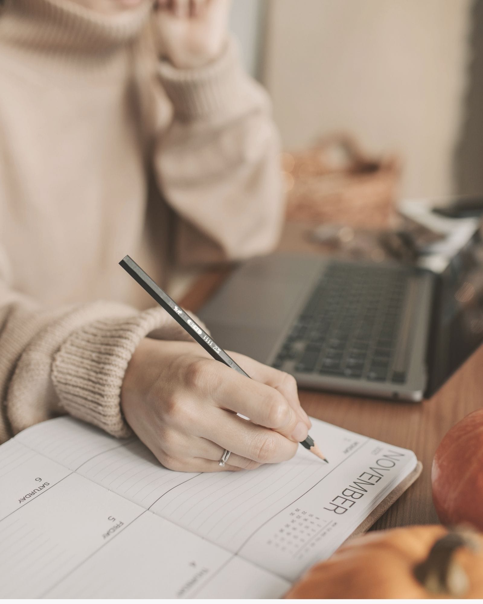 A person writes in a planner at a wooden table, preparing a care schedule in a warm home setting.