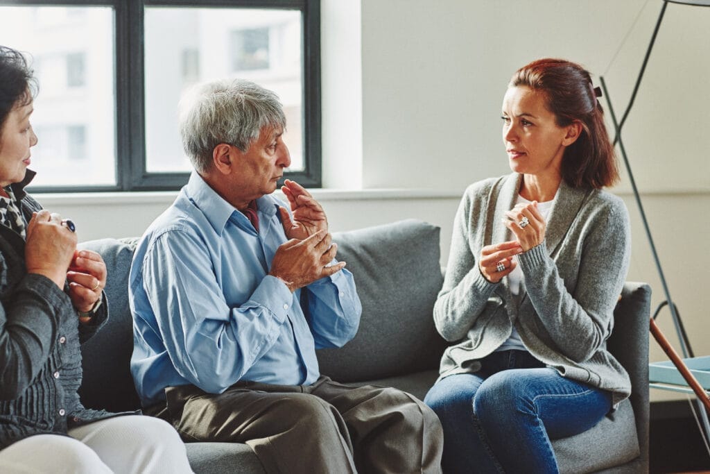 Three people using sign language in a relaxed indoor setting, sharing a moment of accessible and inclusive communication.