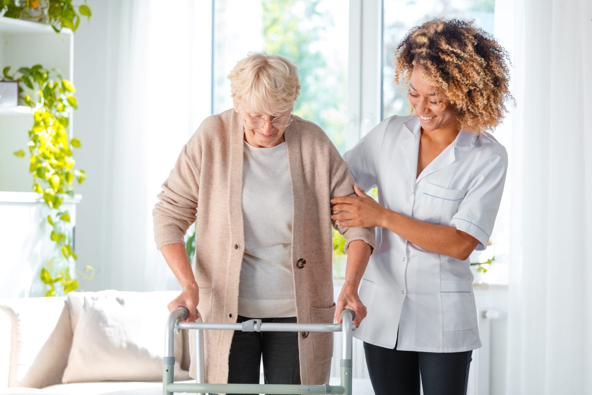 Caregiver gently supporting an older adult with a walker in a bright home setting, providing dignified and reassuring personal care