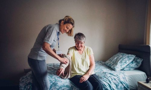 The woman is helping a senior woman dress.