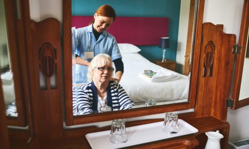 Reflection of happy young woman healthcare worker combing hair of a senior female patient at retirement home